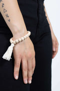 Braccialetto di perle in legno non trattato con frangia in cotone. Colore bianco
