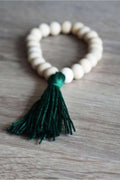 Braccialetto di perle in legno non trattato con frangia in cotone. Colore verde scuro