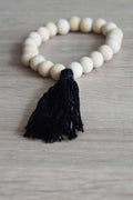 Braccialetto di perle in legno non trattato con frangia in cotone. Colore nero