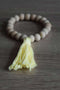 Braccialetto di perle in legno non trattato con frangia in cotone. Colore giallo